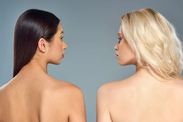 Multiethnic models with bare shoulders looking at each other on blue backdrop, diverse beauty — Stock Photo