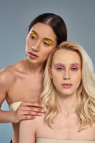 Modelos multiétnicos con maquillaje de ojos audaces posando juntos sobre fondo azul, concepto de belleza diversa - foto de stock