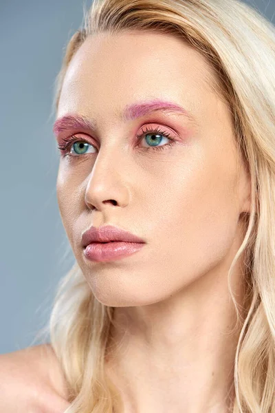 Крупным планом, женщина с розовым макияжем глаз и голубыми глазами, отводящими взгляд на серый задник, женственная красота — стоковое фото