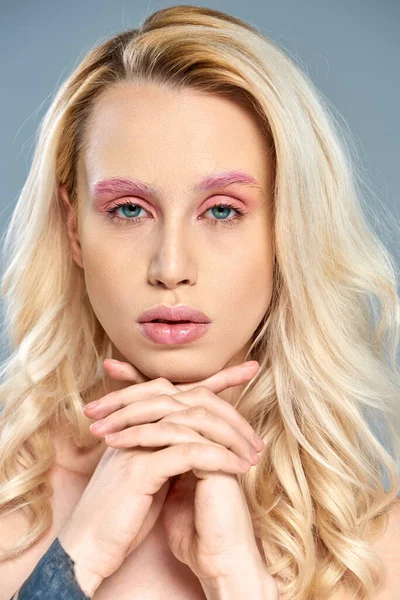 Tätowiertes Model mit rosa Augen-Make-up und blonden Haaren posiert vor grauem Hintergrund, feminine Schönheit — Stockfoto