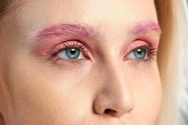 Detailed photo of young woman with blue eyes and pink eyeshadows looking away, close up — Stock Photo