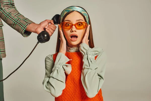 Homme tenant combiné de téléphone vintage près choqué femme de style rétro dans des lunettes de soleil sur gris — Photo de stock
