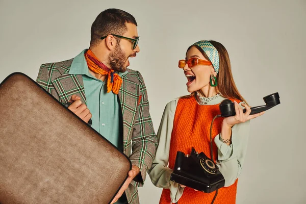 Overjoyed retro style couple with vintage suitcase and corded phone looking at each other on grey — Stock Photo
