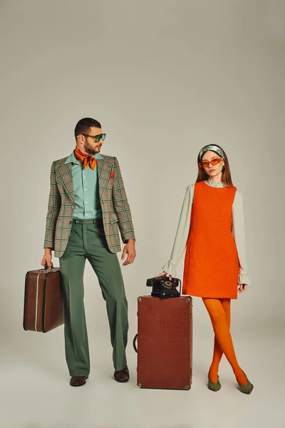 Casal old-fashioned em roupas brilhantes posando com malas vintage e telefone retro em cinza — Fotografia de Stock