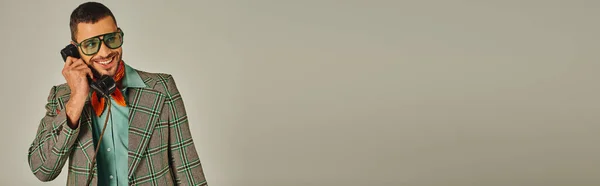 Homme joyeux en veste à carreaux et lunettes de soleil parlant sur téléphone rétro sur gris, mode vintage, bannière — Photo de stock