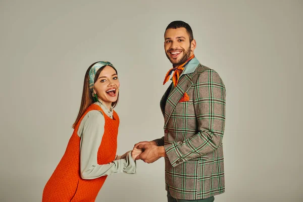 Jeune couple joyeux en tenue vintage élégant tenant la main et regardant la caméra sur fond gris — Photo de stock