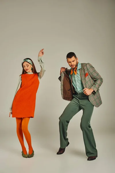 Молодая пара в клетчатой куртке и оранжевом платье танцуют на сером, винтажная мода, полная длина — стоковое фото