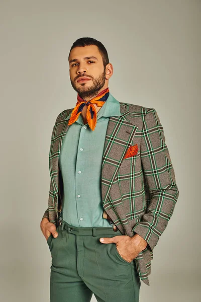 Uomo sicuro di sé in giacca a quadri e coloratissimo fazzoletto in piedi con le mani in tasca sul grigio — Foto stock