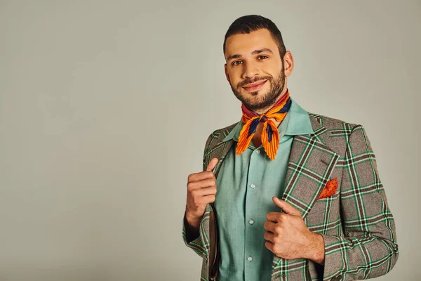 Elegante uomo in blazer a quadretti e coloratissimo fazzoletto sorridente alla macchina fotografica su grigio, moda vintage — Foto stock