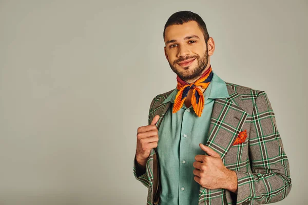 Elegant man in checkered blazer and colorful neckerchief smiling at camera on grey, vintage fashion — Stock Photo