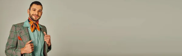 Homme heureux en veste à carreaux et foulard lumineux souriant à la caméra sur gris, style rétro, bannière — Photo de stock
