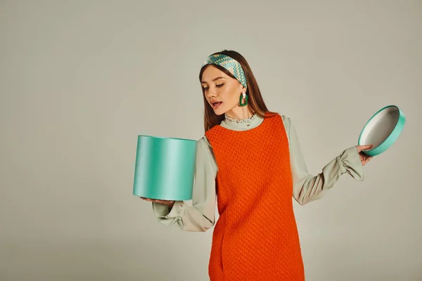 Curiosa donna in abito arancione e fascia in cerca in confezione regalo su grigio, retrò fotografia di moda — Foto stock