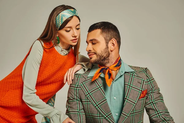 Woman in orange dress leaning on shoulder of man in plaid jacket on grey, stylish vintage couple — Stock Photo