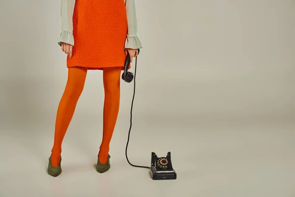 Vista ritagliata della donna in abito arancione e collant con portatile di telefono vintage su grigio, stile retrò — Foto stock