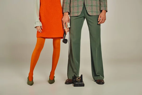 Обрезанный вид на пару в модной ретро-одежде, стоящую с телефоном на сером — стоковое фото