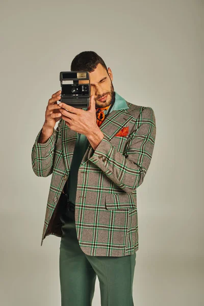 Elegante uomo in giacca a scacchi scattare foto sulla fotocamera vintage su grigio, vecchio stile — Foto stock