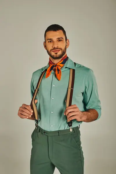 Homme positif dans les bretelles et le foulard coloré regardant la caméra sur gris, style rétro-inspiré — Photo de stock