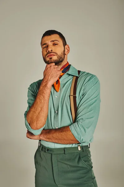 Thoughtful man in suspenders and bright neckerchief looking at camera on grey, vintage fashion — Stock Photo