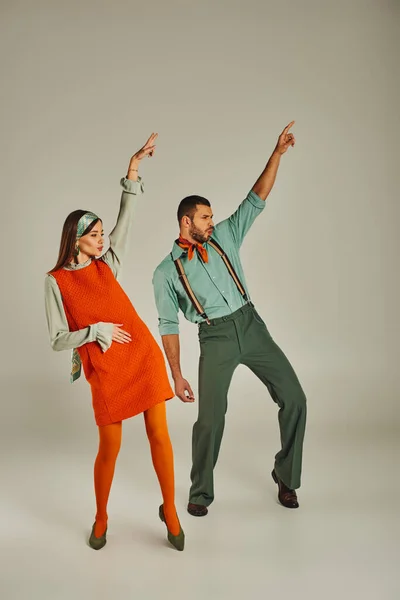 Elegante pareja en ropa vintage bailando con las manos levantadas en gris, vibraciones retro y emoción - foto de stock