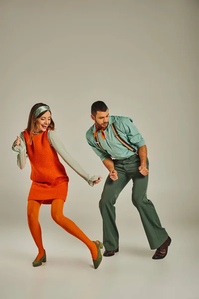 Piena lunghezza di giovane coppia alla moda in abiti retrò colorati ballare sul grigio, divertimento ed eccitazione — Foto stock