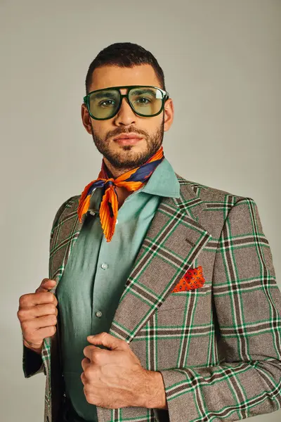 Homme de style rétro en blazer à carreaux et foulard coloré avec des lunettes de soleil regardant la caméra sur gris — Photo de stock