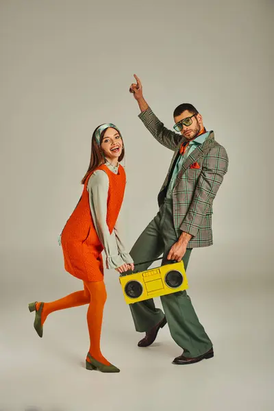 Alegre casal à moda antiga com boombox amarelo dançando em cinza, felicidade e estilo de vida retro — Fotografia de Stock