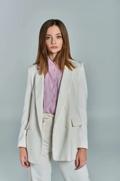 Junge stilvolle Frau im weißen eleganten Anzug mit Blick in die Kamera auf graue, klassisch minimalistische Mode — Stockfoto