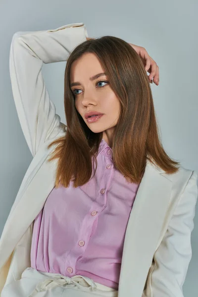 Jeune femme charmante en blazer blanc regardant loin avec la main derrière la tête sur gris, la mode et le style — Photo de stock