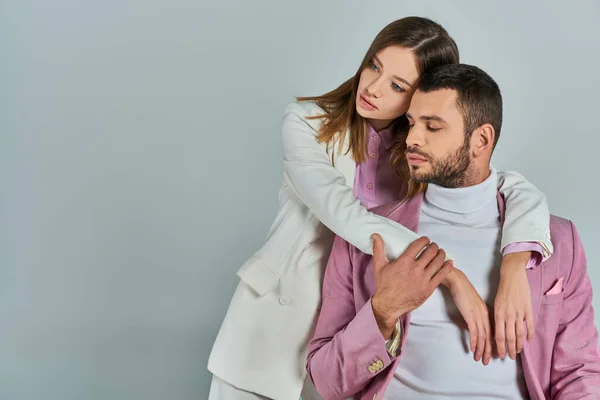 Mujer joven en traje blanco abrazando al hombre en blazer lila en gris, pareja con elegante atuendo formal — Stock Photo