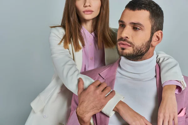 Mulher em roupas de negócios elegantes abraçando homem pensativo em blazer lilás olhando para longe em cinza — Fotografia de Stock
