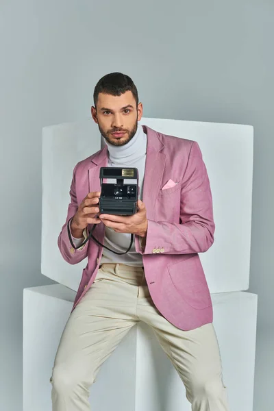 Homem bonito e elegante em blazer lilás segurando câmera vintage perto de cubos brancos em fundo cinza — Fotografia de Stock
