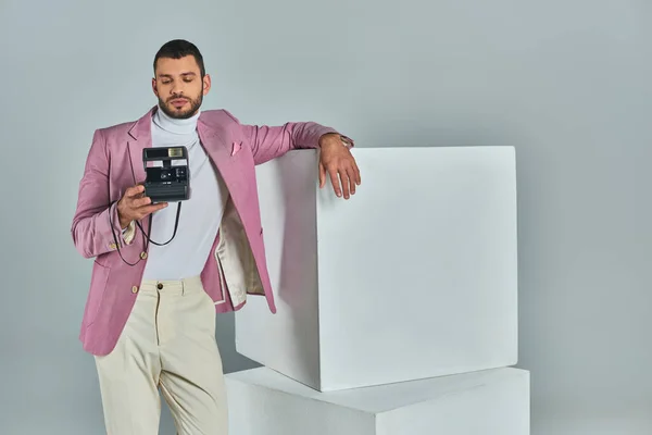 Jeune homme en tenue formelle élégante posant près de cubes blancs avec caméra vintage sur gris, mode moderne — Photo de stock