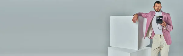 Homme à la mode en tenue de travail debout près de cubes blancs avec caméra vintage sur gris, bannière — Photo de stock