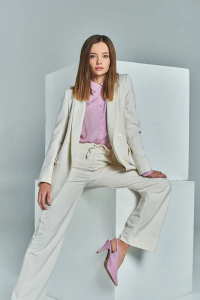 Attraktive Frau im eleganten Anzug posiert neben weißen Würfeln auf grauer, minimalistischer Businessmode — Stockfoto