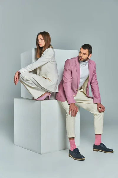 In voller Länge junge modische Paar in eleganter formeller Kleidung posiert auf weißen Würfeln auf grau — Stockfoto