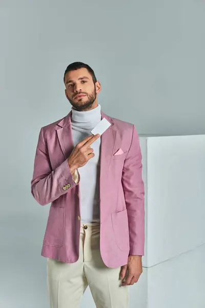 Homme d'affaires élégant et confiant en blazer lilas tenant une carte de visite vierge près de cubes blancs sur gris — Photo de stock