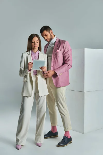 Jeune couple d'affaires en tenue formelle élégante regardant tablette numérique près de cubes blancs sur gris — Photo de stock