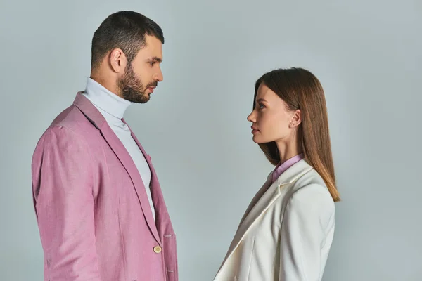 Vista laterale di giovane coppia in blazer alla moda guardarsi l'un l'altro su grigio, moda minimalista — Foto stock
