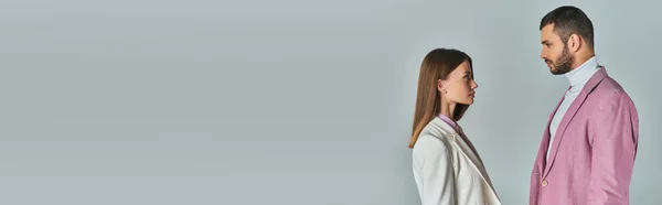 Seitenansicht eines jungen Paares in stylischen Blazern, die sich auf grau, Businessmode, Banner anschauen — Stockfoto