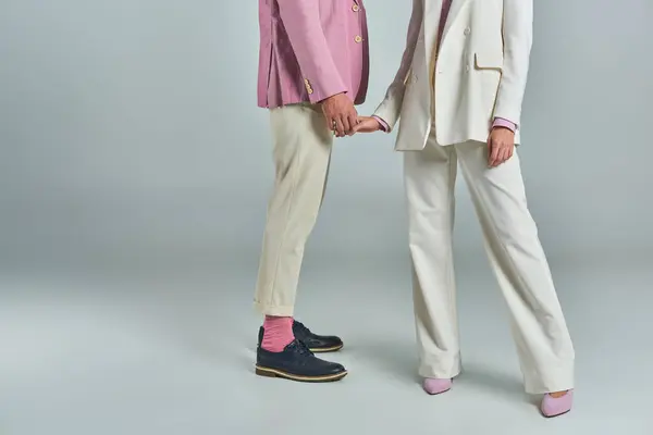 Vista recortada de pareja moderna en traje formal de moda de pie y cogidas de la mano sobre fondo gris - foto de stock