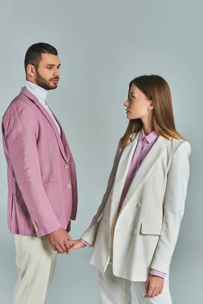 Young fashionable couple in pastel business attire holding hand and looking at each other on grey — Stock Photo