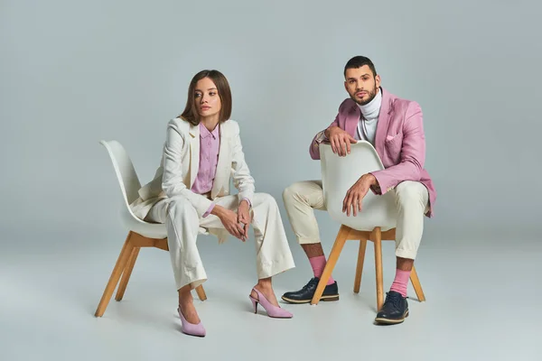 Trendy business couple in pastel formal wear sitting in armchairs on grey, minimalistic fashion — Stock Photo