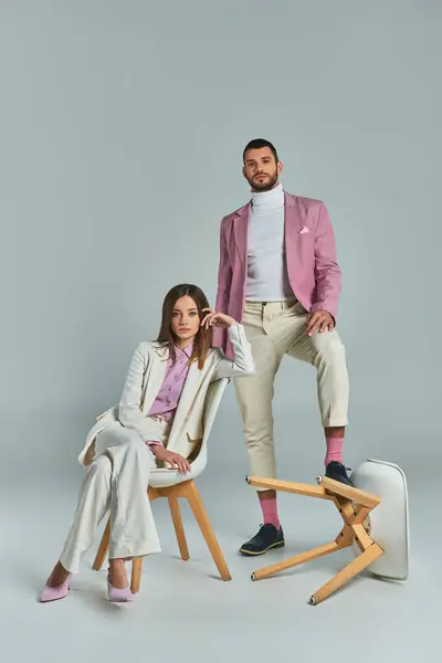 Fashionable couple in elegant formal wear posing with armchairs on grey, modern business fashion — Stock Photo