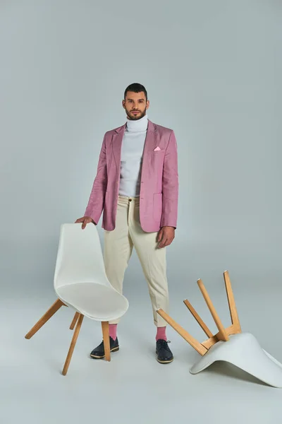 Longueur totale de l'homme en blazer lilas et pantalon blanc posant avec des fauteuils sur gris, mode et style — Photo de stock