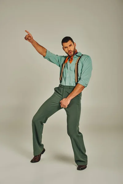 Excité homme en vêtements rétro et bretelles pointant du doigt et dansant sur gris, pleine longueur — Photo de stock