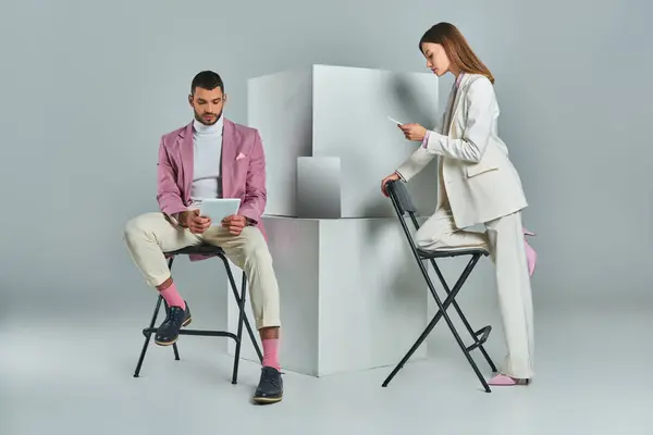 Casal elegante usando smartphone e tablet digital perto de laptop em cubos brancos em pano de fundo cinza — Fotografia de Stock