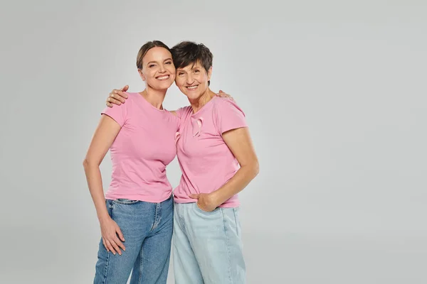 Conceito de câncer de mama, feliz duas mulheres olhando para a câmera, abraço e sorriso, fundo cinza, suporte — Fotografia de Stock