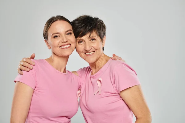 Concepto de cáncer de mama, felices dos mujeres mirando a la cámara y abrazándose en el fondo gris, apoyo - foto de stock