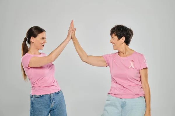 Концепция рака молочной железы, счастливые женщины с розовыми лентами давая пять на сером фоне, рак бесплатно — стоковое фото