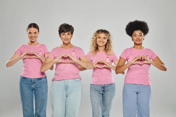 Brustkrebs-Bewusstsein, glückliche interrassische Frauen mit rosafarbenen Bändern, die Herz auf Grau zeigen, Vielfalt — Stockfoto